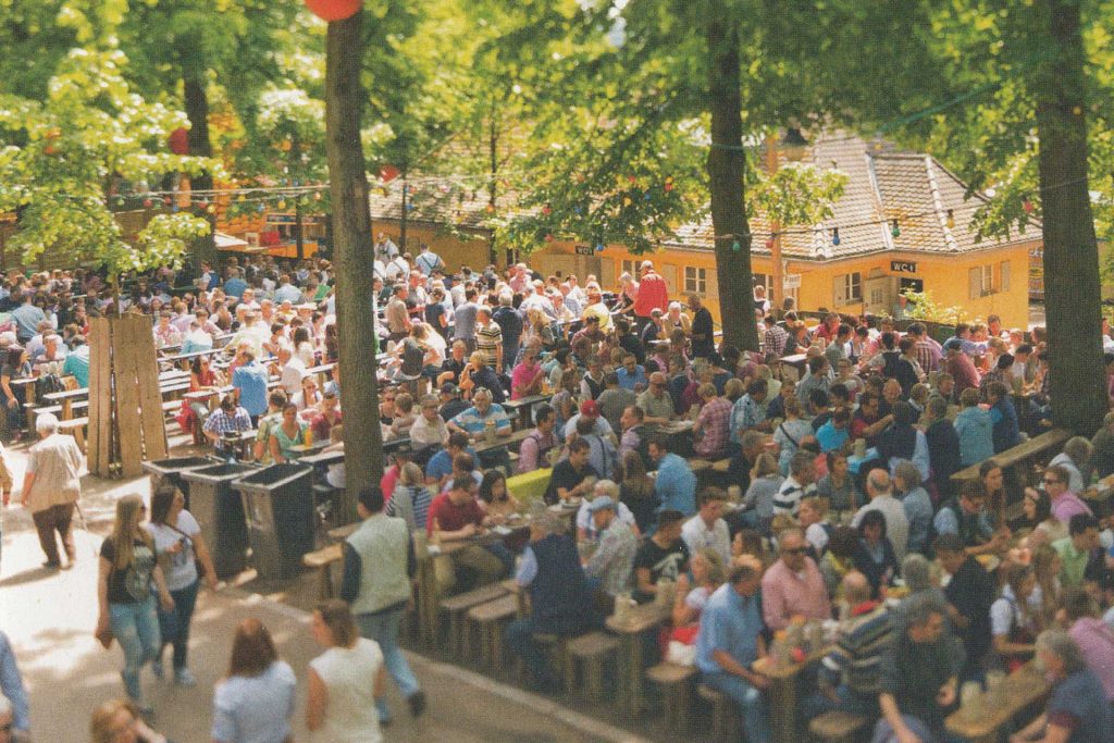 Besucher der Erlanger Bergkirchwei sitzen auf Bierbänken unter Bäumen